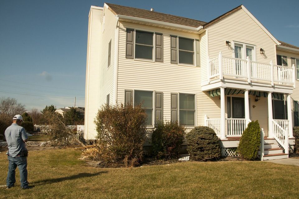 Inspector with a clipboard looking over a two-story house with vinyl siding