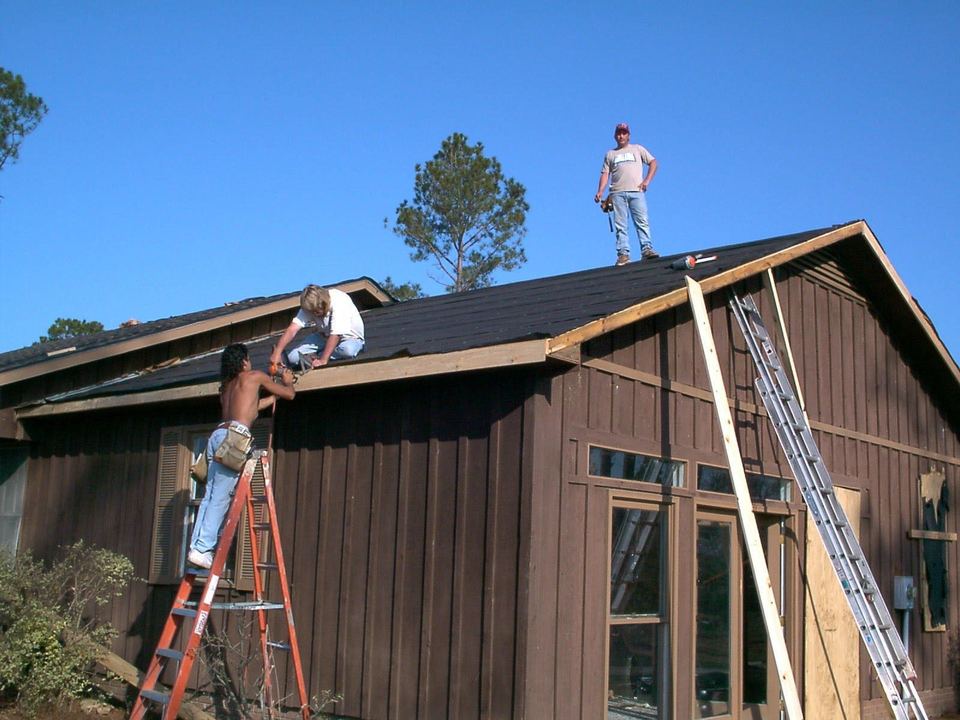 Roofers on a ladder and the ridge putting a new roof on a wooden house