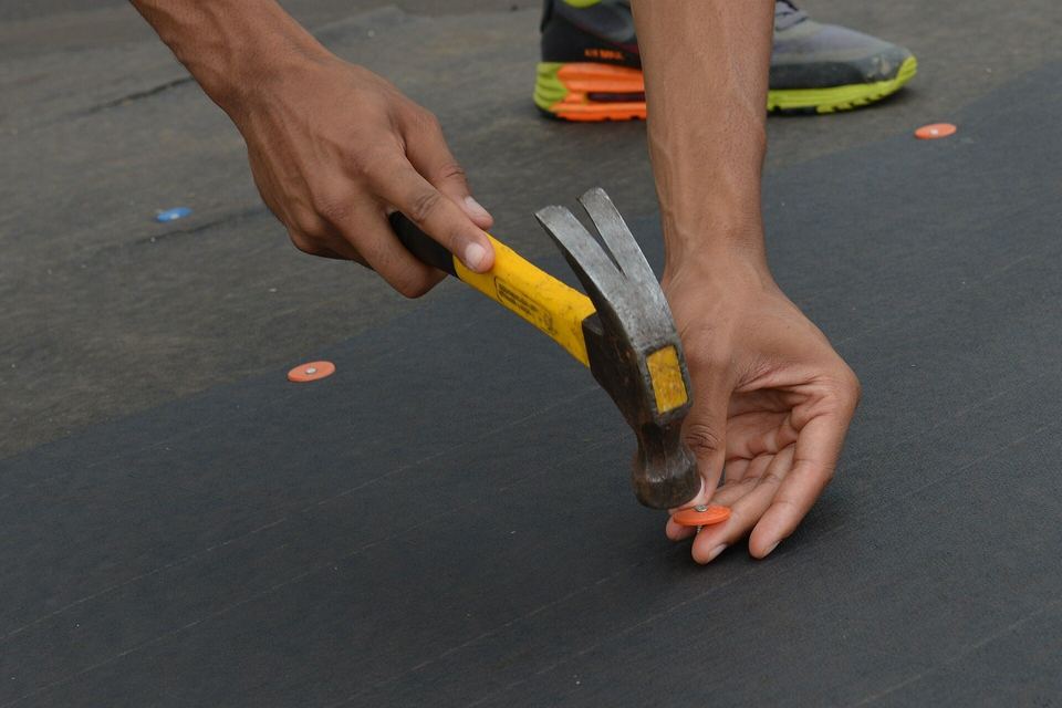 Hands hammering a plastic cap nail into dark roof underlayment